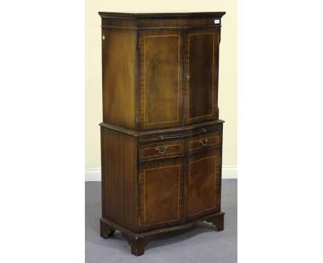 A late 20th Century reproduction mahogany serpentine fronted drinks cabinet, the moulded pediment above a pair of doors revea