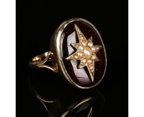 A gold, carbuncle garnet and seed pearl ring, the oval garnet centred by a seed pearl set starburst motif between split shoul