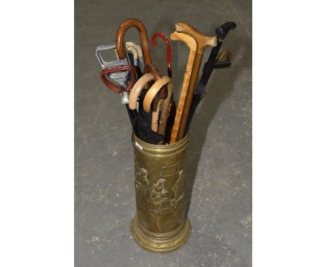 A brass stick stand with a collection of sticks and umbrellas, the embossed cylindrical brass stick stand containing eighteen