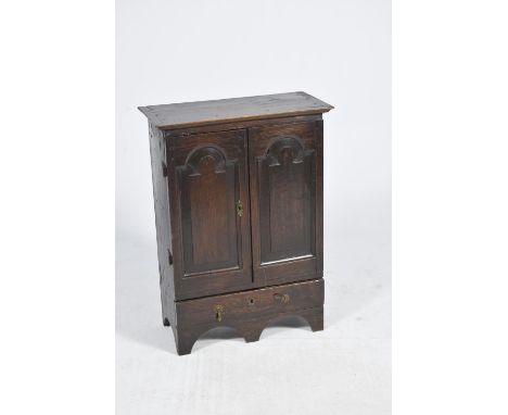 An 18th century oak spice cupboard,Having fielded paneled cupboard doors enclosing a single shelf above a freeze drawer, rais