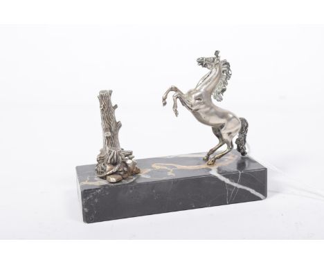 A 1930's white metal desk ornament, modeled as a rearing horse in front of a tree trunk cast with a coiling snake, upon a rec