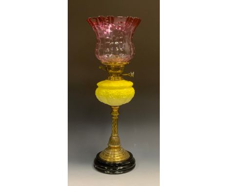 A Victorian brass and yellow milk glass oil lamp, cranberry glass shade above relief decorated yellow reservoir, brass column