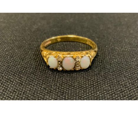 A diamond and opal ring, set with three oval opal cabochons each divided by a pair of diamond accents. 18ct gold shank, size 