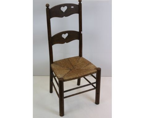 In the manner of Liberty of London, Arts and Crafts Oak Ladder Back Chair with pierced heart motifs and rush seat, 48cm wide 