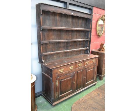 A George III oak dresser, three shelves and shaped uprights to top, short faux drawer flanked by two long over fielded panel 