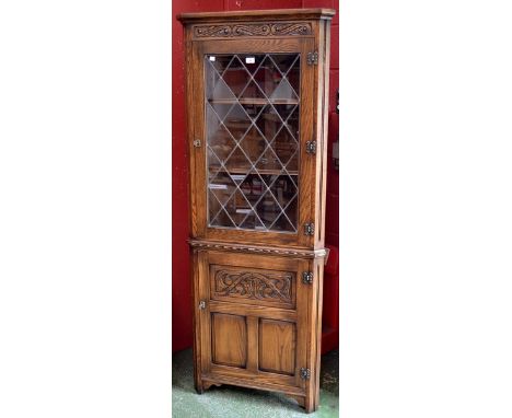 An Old Charm style oak tall corner cabinet, carved pediment, glazed door to top, carved oak panelled door to base, 184cm tall