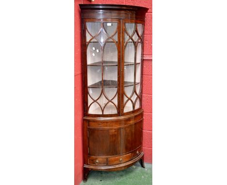 A mahogany bowfront floor standing corner cabinet, stepped cornice, two astragal glazed doors enclosing shelving to top, two 