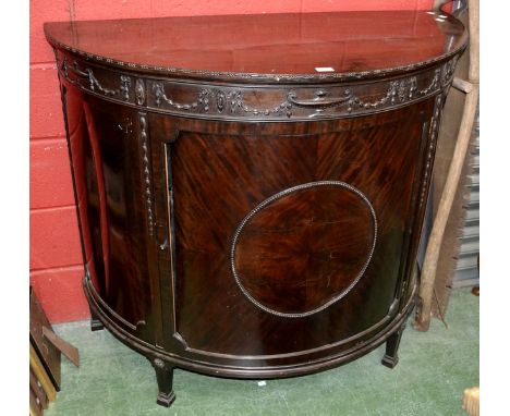 A Regency style demi-lune cabinet, dot and dash beaded top, urns, swags and bows carved in relief to frieze, single crossband