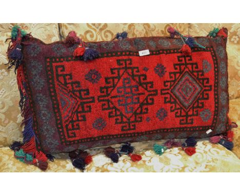 A mid to late 20th century carpet cushion in tones of red and black, tassel fringe