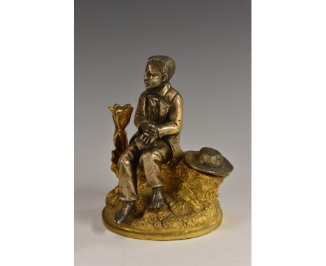 A 19th century gilt and silvered bronze novelty inkwell, cast as a well dressed young man, seated on a tree trunk, his straw 