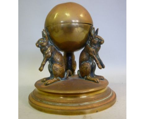 An early 20thC brass novelty inkwell, fashioned as a sphere, the lid enclosing a reservoir, elevated by three standing hares,