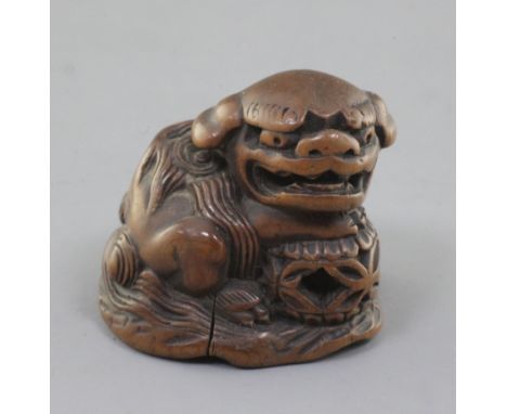 A Japanese wood netsuke of a shishi, seated on a rock, 19th century, its paw and chin resting upon a brocaded ball, two chara