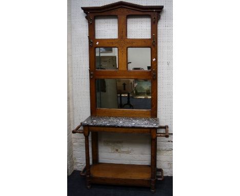 An Edwardian oak hallstand, the architectural pediment over partially mirrored back with six brass hooks, marnle shelf, on ri