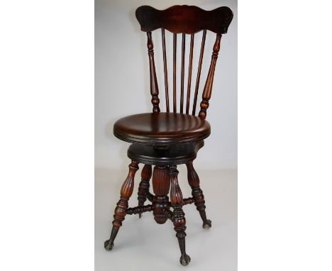 An early 20th century American piano chair, with eared rail, stick splats, circular adjustable seat, on lobed splayed support