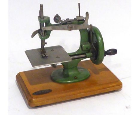 CHILD'S 'GRAIN' MANUAL SEWING MACHINE with green cast iron G shaped frame, mounted on an oblong wooden base with a metal oval