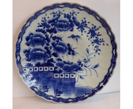 A large Japanese porcelain charger, scalloped edge and hand decorated in underglaze blue with a single bird in flight approac
