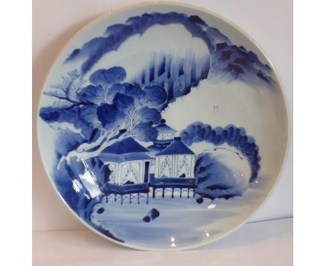 A late 19th/early 20th century Japanese porcelain dish decorated in underglazed blue with two buildings before water and moun