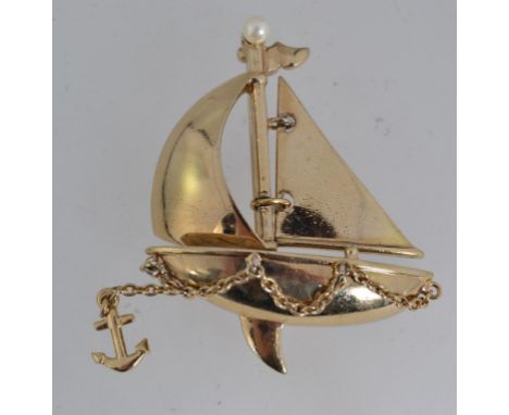 A vintage yellow metal figural brooch pin in the form of a sailing boat with articulating sail and dangle chain anchor with p