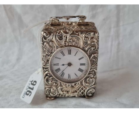 An embossed silver cased travelling clock, decorated with scrolls, swing handle and bun feet, 4" over handle, Birmingham 1906
