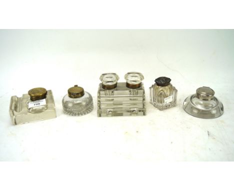 A collection of five glass inkwells, of various designs, three with brass tops, one being a dual inkwell, the largest measuri