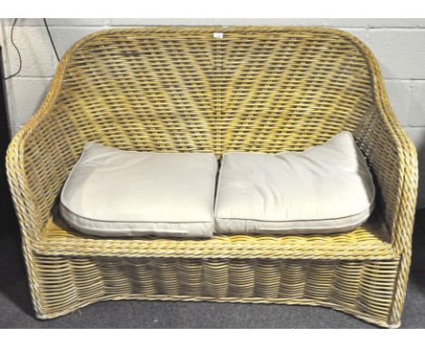 A contemporary wicker sofa, with a curved back and two cream cushions, 90cm x 137cm x 80cm
