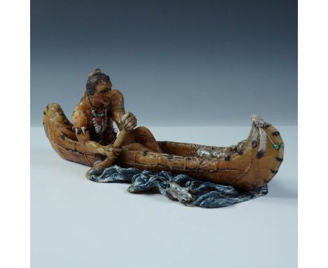 A detailed figural resin sculpture depicting a Native American man paddling a canoe through stylized waters. The figure is ad