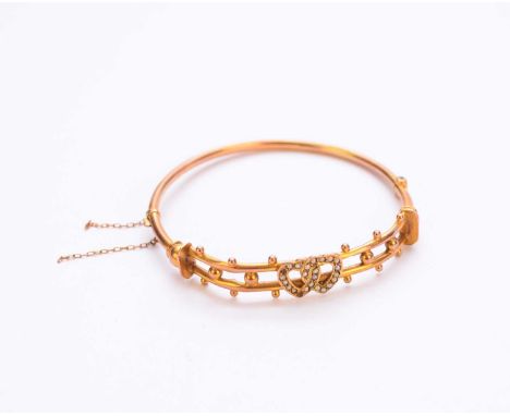 An early 20th century split seed pearl set bangle, the entwined seed pearl hearts mounted to yellow metal openwork bead embel