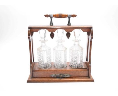 A late Victorian Oak and electroplated mounted tantalus with a locking handled top above three cut glass decanters, 35.5cm wi