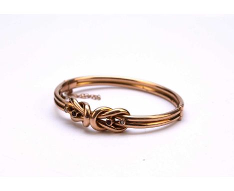 A seed pearl and red paste hinged bangle, the yellow metal bangle of stylised knot form set with two split seed pearls and tw