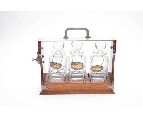 A late Victorian oak three-decanter tantalus, with polished steel bracket and carrying handle, with three cut glass decanters