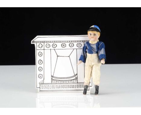 An all-bisque dolls’ house jockey, with blue painted eyes, blonde moulded and painted hair, moulded cap with light and dark b