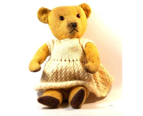 A 1940s Chiltern gold plush teddy bear 
With glass buttons eyes and articulated limbs, in white knitted dress, height 38cm.