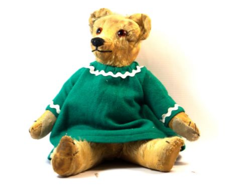 A 1920s Chad Valley gold plush teddy bear
With button to right ear, glass eyes and articulated limbs in green dress, height 3