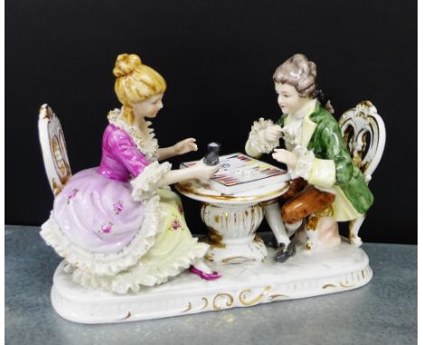 A continental porcelain figure of a Male and Female figure group, each modelled seated, whilst playing Backgammon, 26cm long