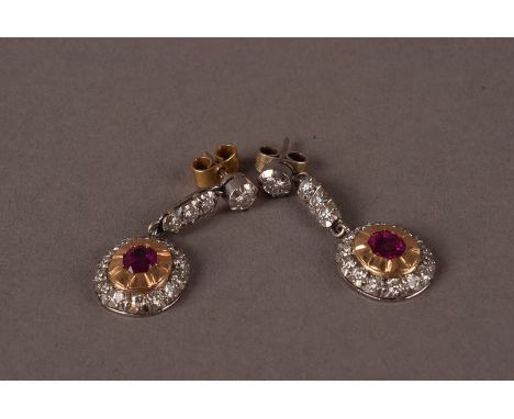 A vintage pair of diamond and ruby pendant earrings, having a drop cluster centre with an oval cut red stone in gold surround