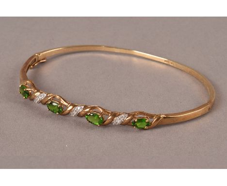 A 9ct gold and gem set bangle, the twist style central panel set with four oval green stones, possibly peridot, and set with 