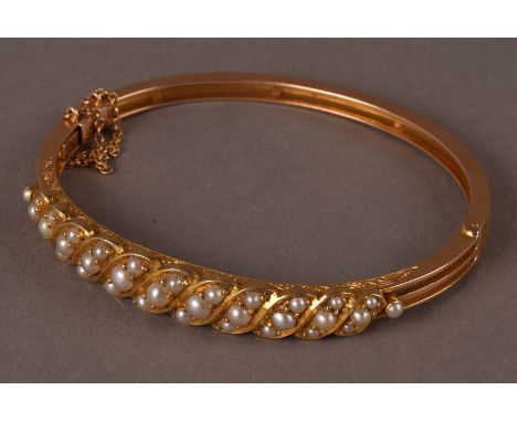 An Edwardian gold and pearl bangle, one half of the hinged oval bangle with rope twist set with small white pearls and engrav