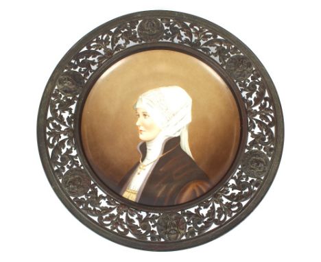 A 19th Century German porcelain plaque, decorated with portrait study of a nun, within pierced cast foliate and mask decorate