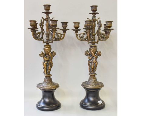 A Pair of Patinated Figural Six Light Candelabra, the pedestals formed as a pair of embracing putti, and on ebonised socles, 