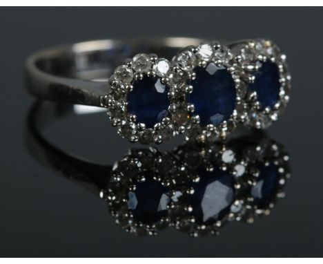 An 18ct white gold, three stone sapphire and diamond ring. Size M. 3.12g.  