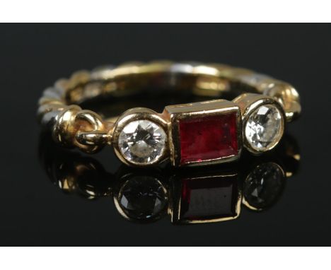 An 18ct yellow and white gold ruby and diamond ring. The central square cut ruby flanked by two brilliant cut diamonds. Havin