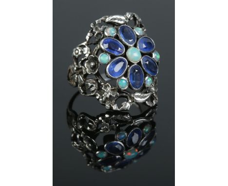 An Arts &amp; Crafts silver ring of floral design, set with sapphire coloured and opal stones. Size P. 6.86g.  Some sapphire 