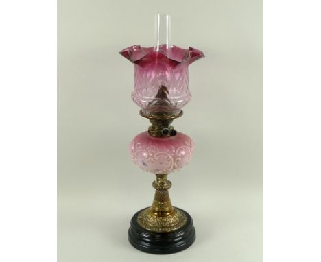 An oil lamp with a cranberry glass shade, a pink ceramic well, brass stem and turned slate base, 19th century, later converte