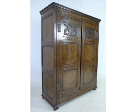 An 18th century oak two door cupboard, cornice over two full length panelled doors carved with scrolls and trefoil leaves, ir