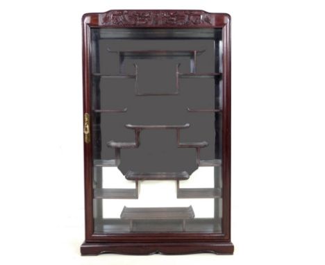 A modern Chinese hardwood display cabinet, carved with opposing dragons, glazed door and mirror back, includes a support shel