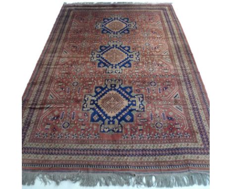 An Afghan hand knotted wool carpet with geometric motifs and guls on a dark red ground, three dark blue medallions, multiple 