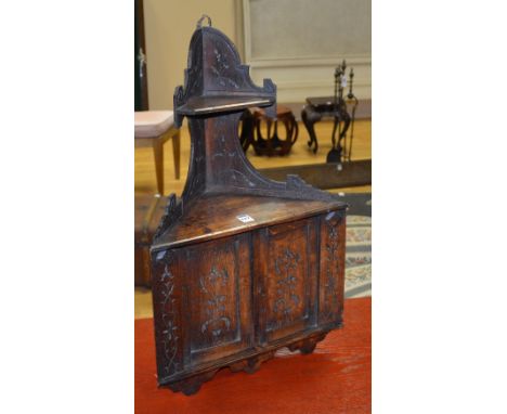 An oak wall mounting corner cabinet, with raised shelf above cupboard doors to front, applied with foliate motifs, 66cm high 