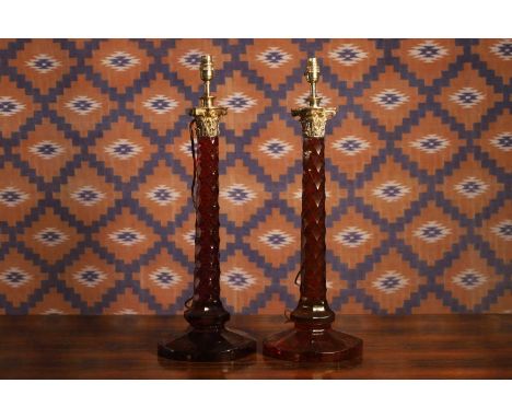 A pair of red glass table lamps, with a gilt brass Corinthian capital, to a facet cut stem, on a star cut circular base, 57cm