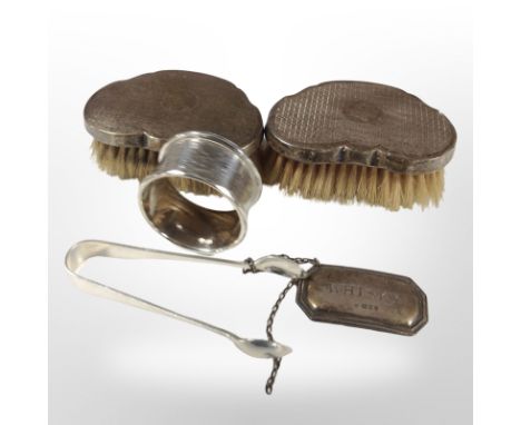 Two silver-backed dressing table brushes, a napkin ring, a pair of sugar tongs, and a whisky decanter label. CONDITION REPORT