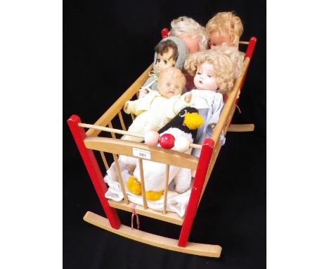 A VINTAGE WOODEN DOLLS COT, containing a quantity of vintage dolls